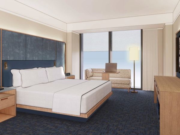 A modern hotel room features a double bed, nightstands, a sofa, a desk lamp, and wall art with large windows providing natural light.