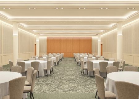 The image shows an empty banquet hall with multiple round tables and chairs, cream-colored walls, and a patterned carpet.