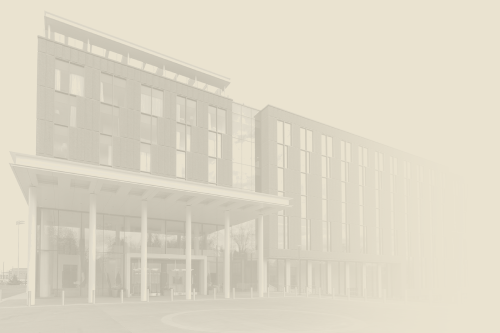 A modern multi-story brick-and-glass building with a covered entrance and tall windows, set in a light, faded backdrop.